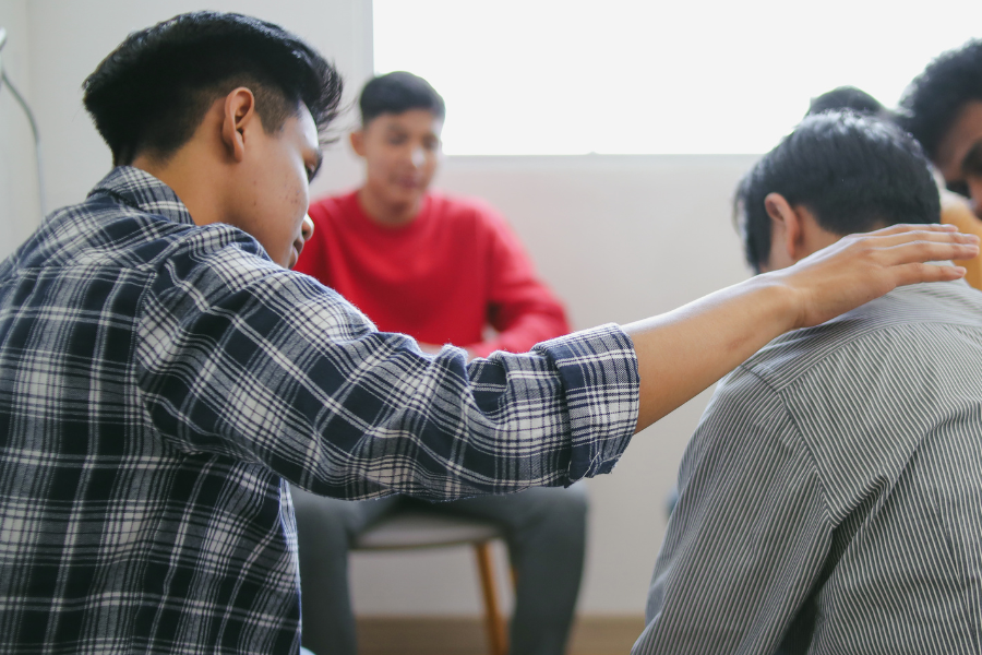 a group of people sit in a meeting circle while one gives a comforting hand to another